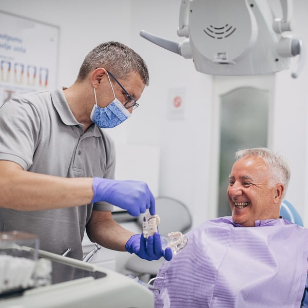 An elderly man sits in a dental chair and smiles.